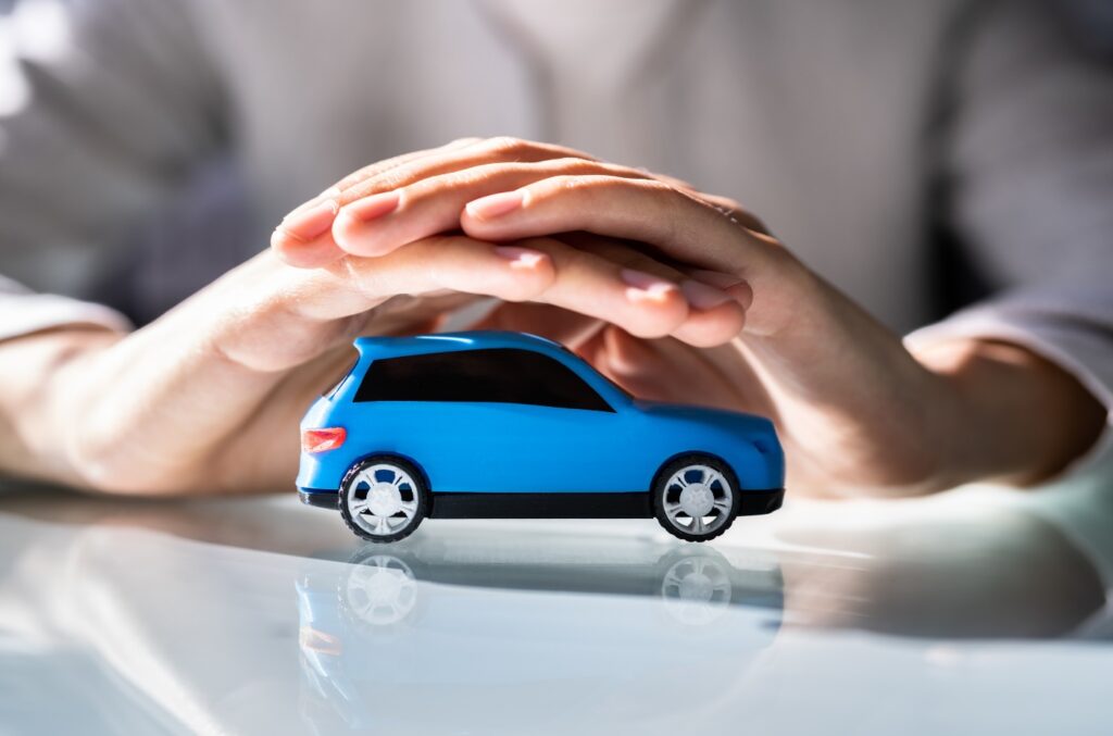 To hender som holder over en blå minatyrbil, illustrerer valg av beste og billigste bilforsikring